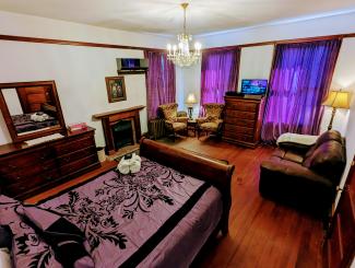 Queen bed, purple curtains, vanity with mirror, couch, wood floors